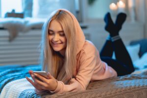 Pretty blond girl in pink using a smart phone lying on the bed a