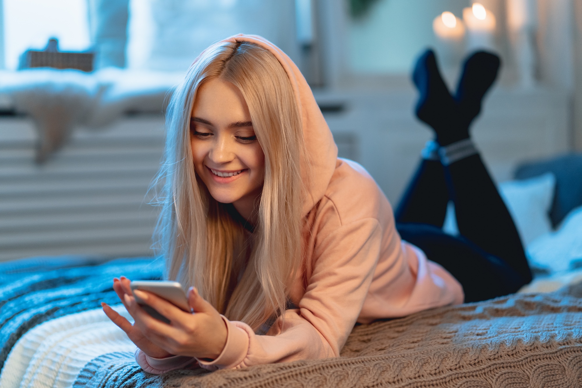 Pretty blond girl in pink using a smart phone lying on the bed a