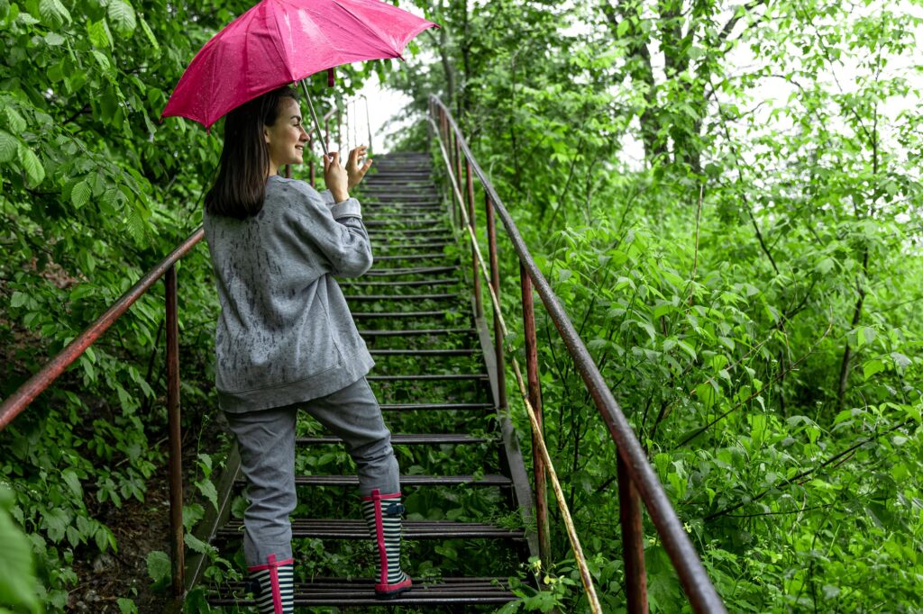 A girl walks in the forest with an umbrella in rainy weather.