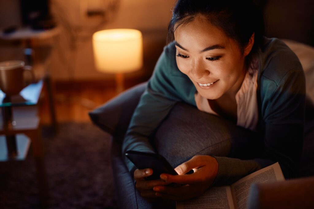Happy Asian woman text messaging on mobile phone in the evening at home.