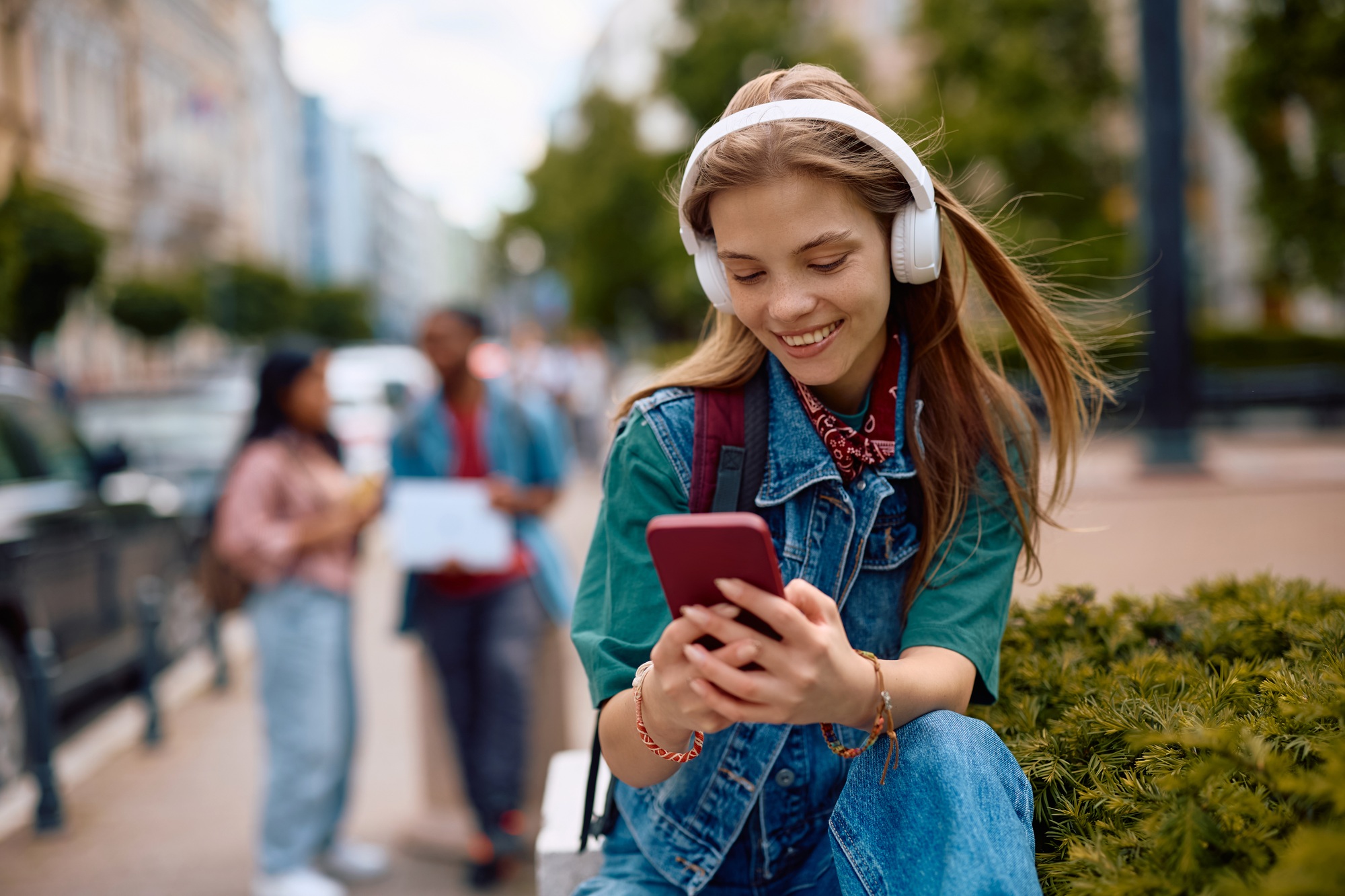 Happy female student text messaging on cell phone outdoors.